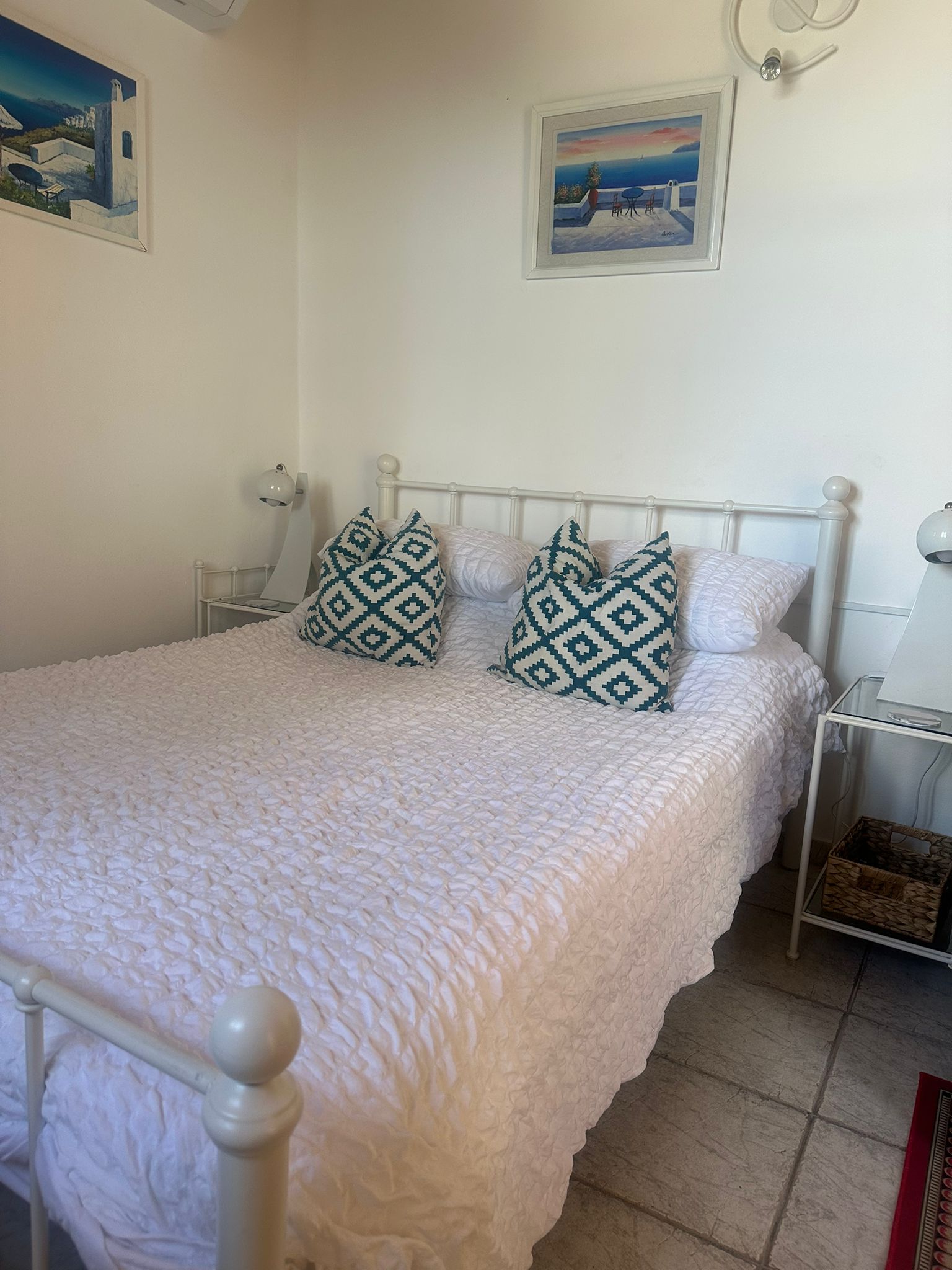 A white double bed with a white cover and blue patterned cushions.