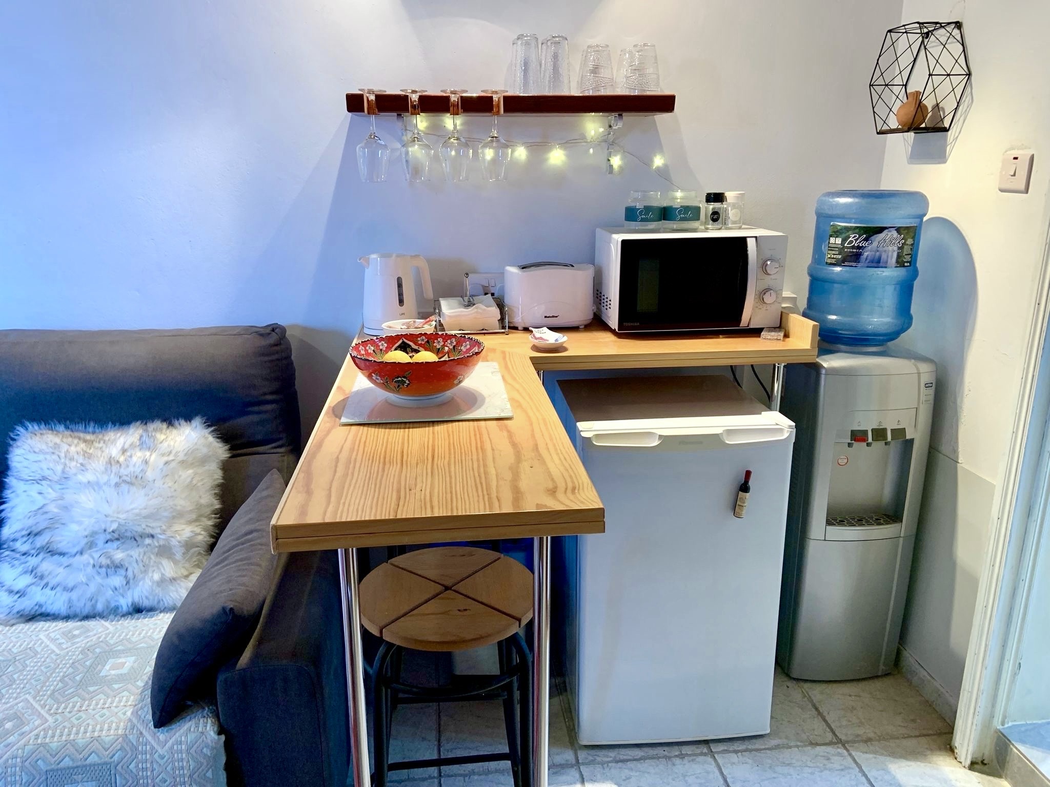 A wooden breakfast bar beside a kitchenette with a microwave, compact fridge, and water dispenser.